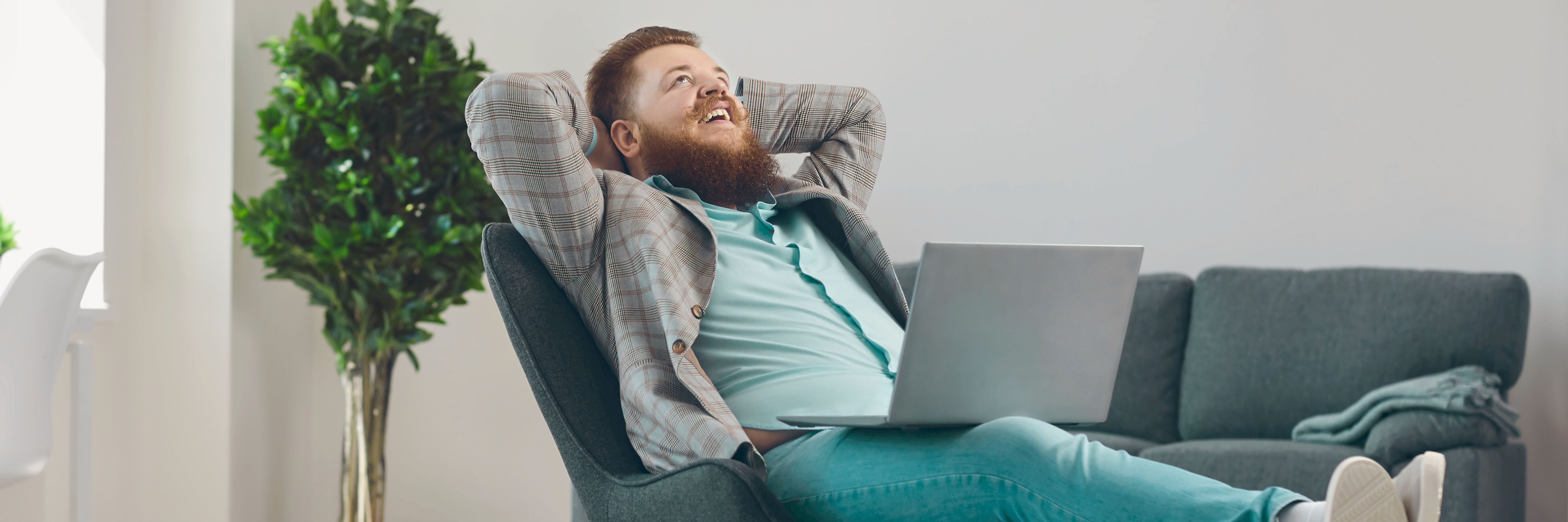 Entspannt zum eigenen Webprojekt. Träume leben Mann entspannt mit Laptop auf dem Schoss im Wohnzimmer. Symbolbild für digitale Freiheit und persönliche Projekte