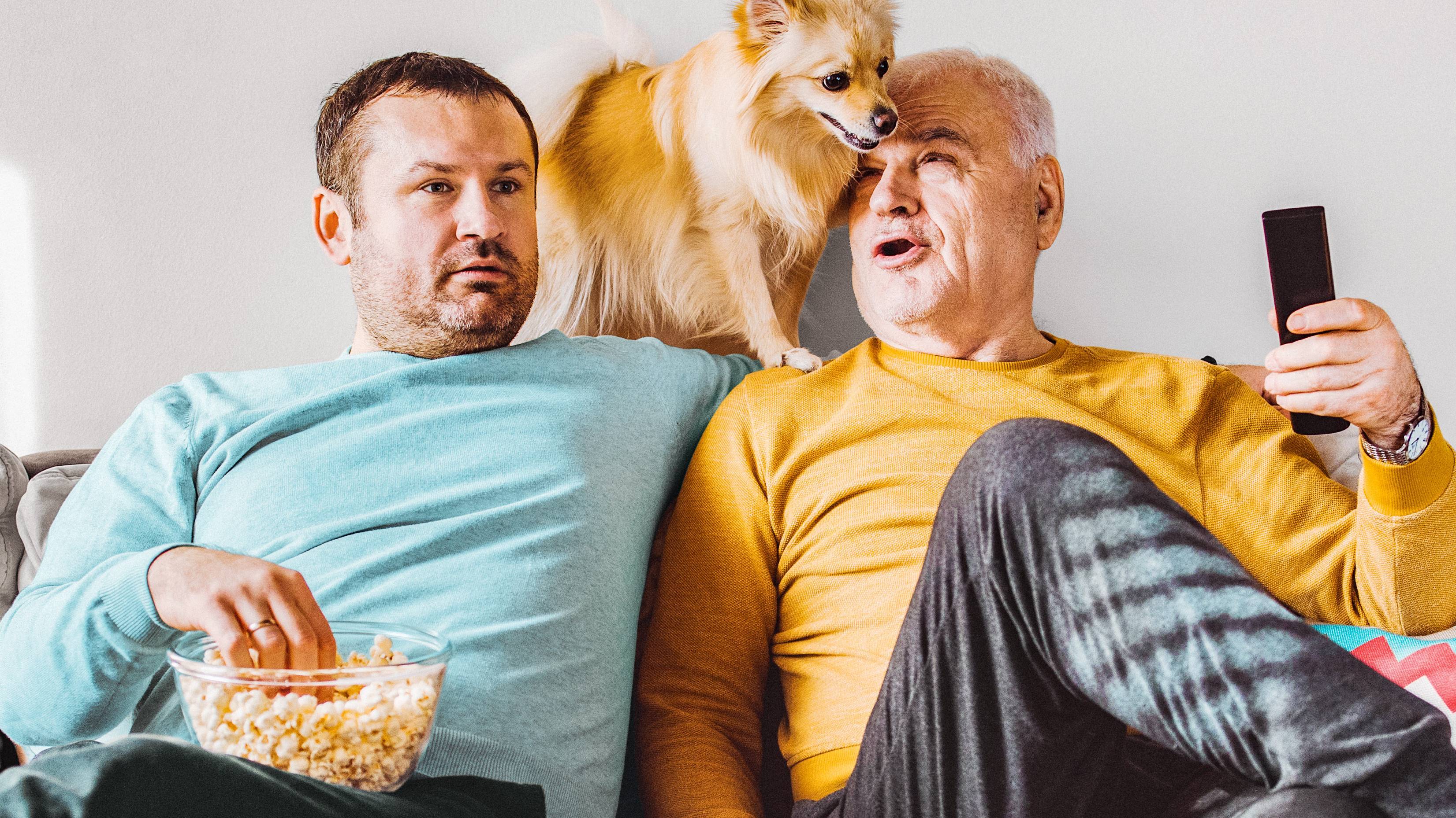 Two friends and their dog are watching TV together.