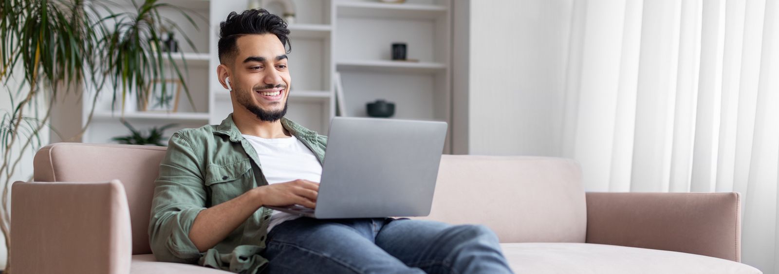 Junger Mann sitzt auf dem Sofa mit einem Laptop