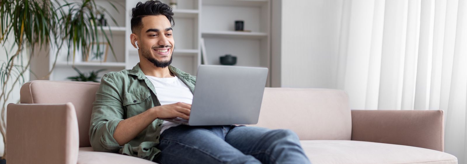 Junger Mann sitzt auf dem Sofa mit einem Laptop